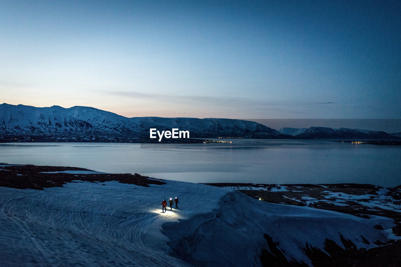 A group of 3 people skis at sunrise with ocean and mountains behind