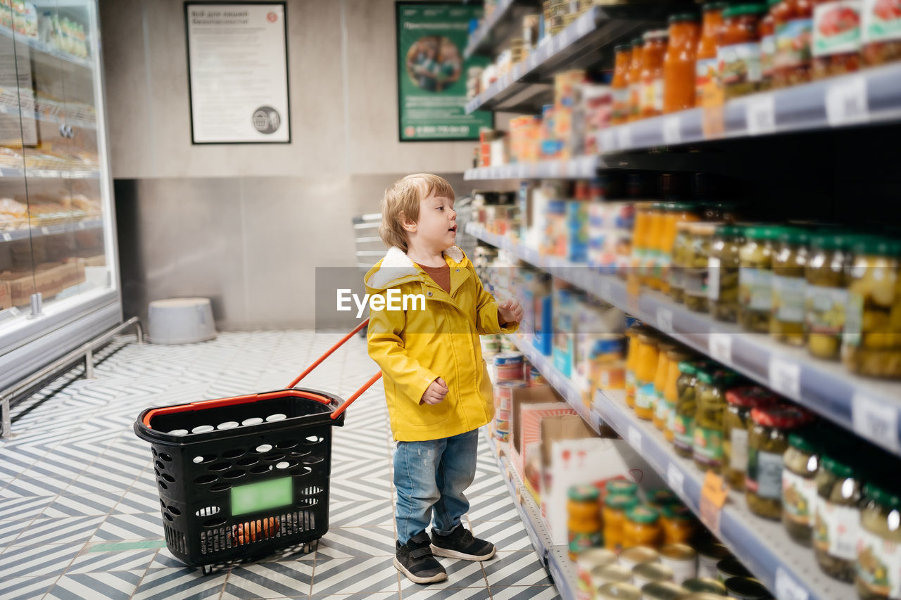 supermarket, shopping cart, retail, store, childhood, shopping, one person, full length, child, groceries, consumerism, customer, blond hair, women, indoors, food and drink, food, grocery store, female, standing, domestic life, casual clothing, building, shelf, lifestyles, aisle, looking, choosing, adult, men, holding, toddler, routine, cute, wellbeing, variation, market, pushing, healthy eating, appliance