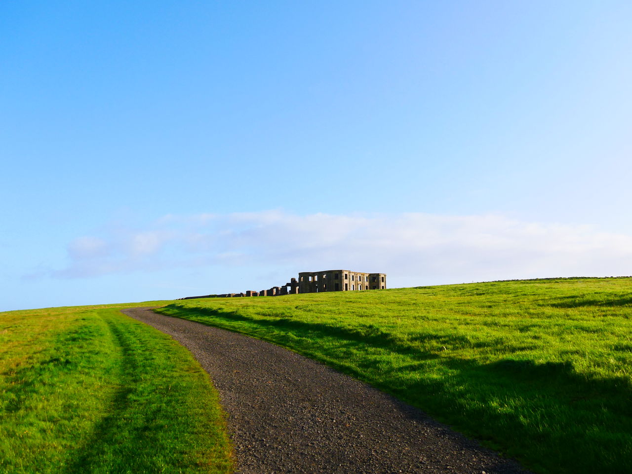 Dirt road amidst field against sky