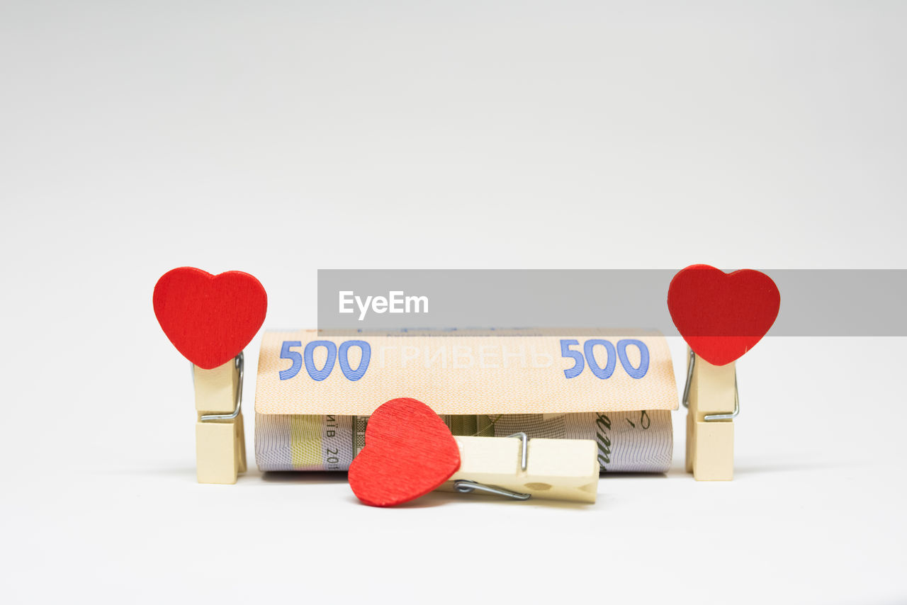 Close-up of paper currency with heart shapes and clothespins on white background