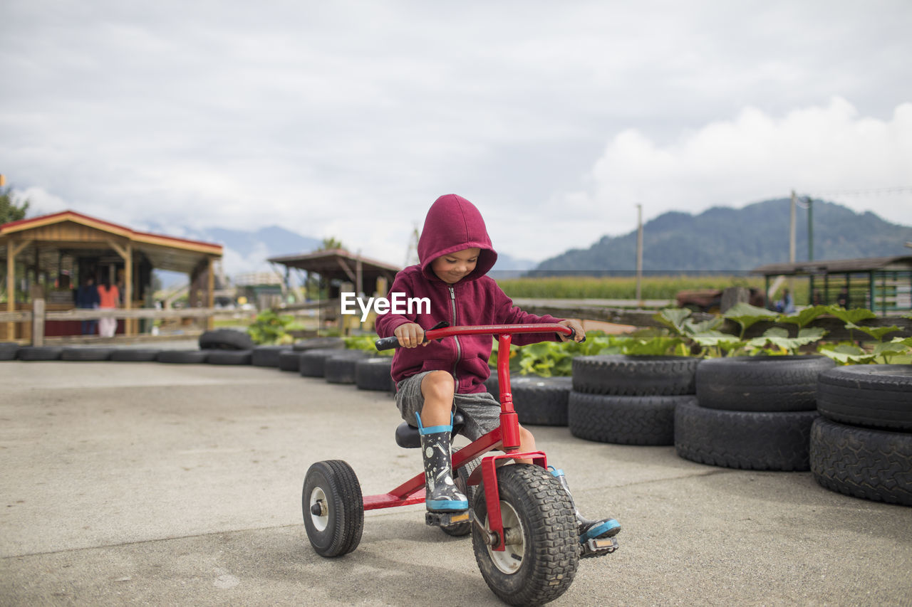 Young boy wearing hoody pedals oversized tricycle on racetrack.
