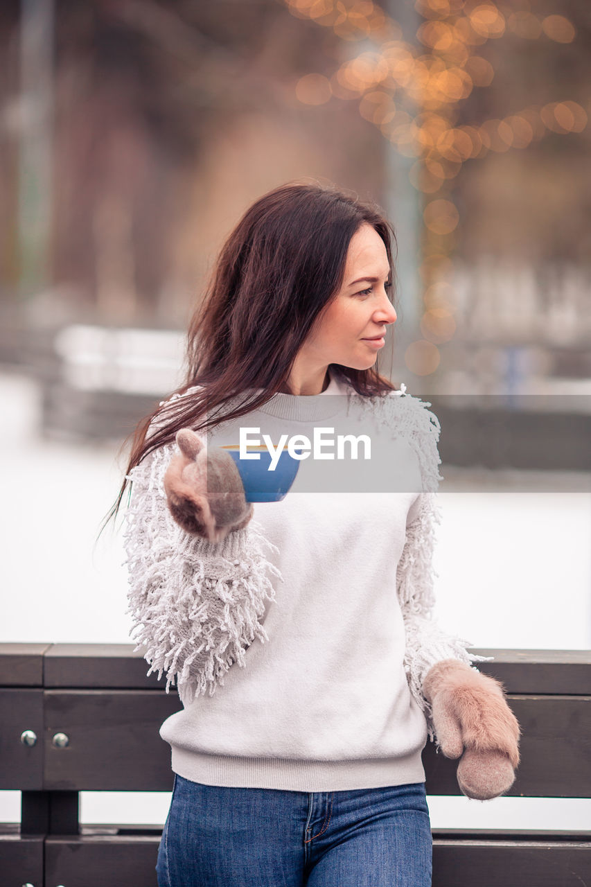 young woman looking away while standing in city