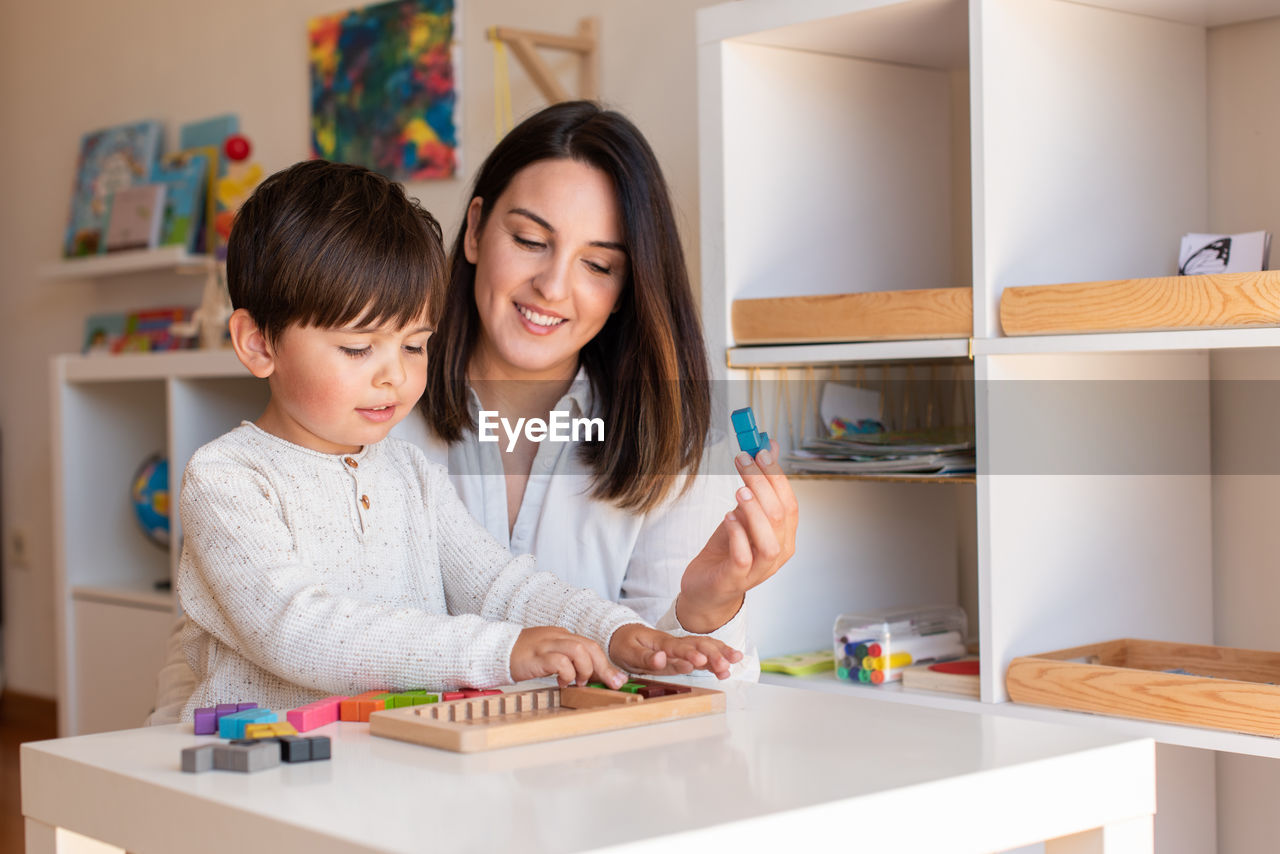 Mother assisting son in puzzle sitting at home