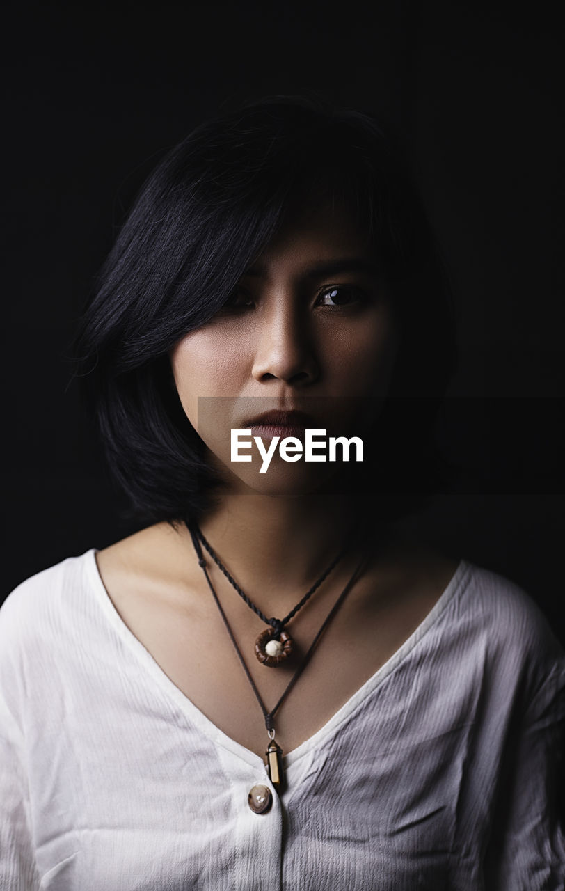 Portrait of young woman against black background