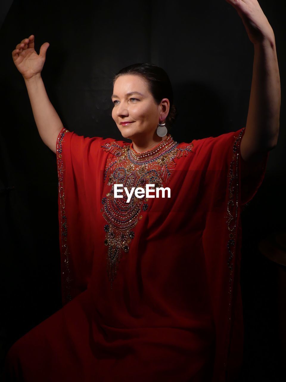 Smiling mature woman wearing red dress while standing against black background