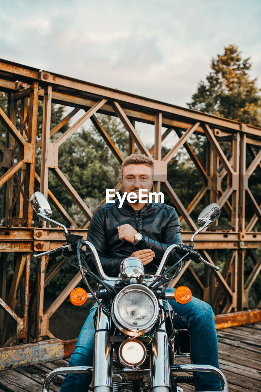 Portrait of man sitting on motorcycle over bridge