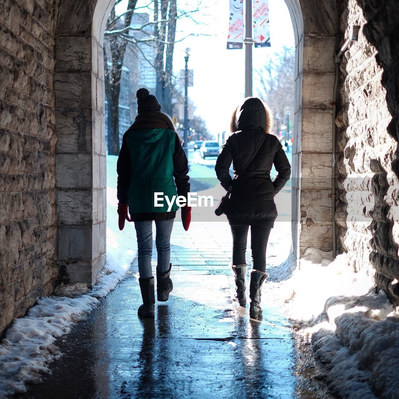 REAR VIEW OF TWO PEOPLE WALKING ON SNOW COVERED