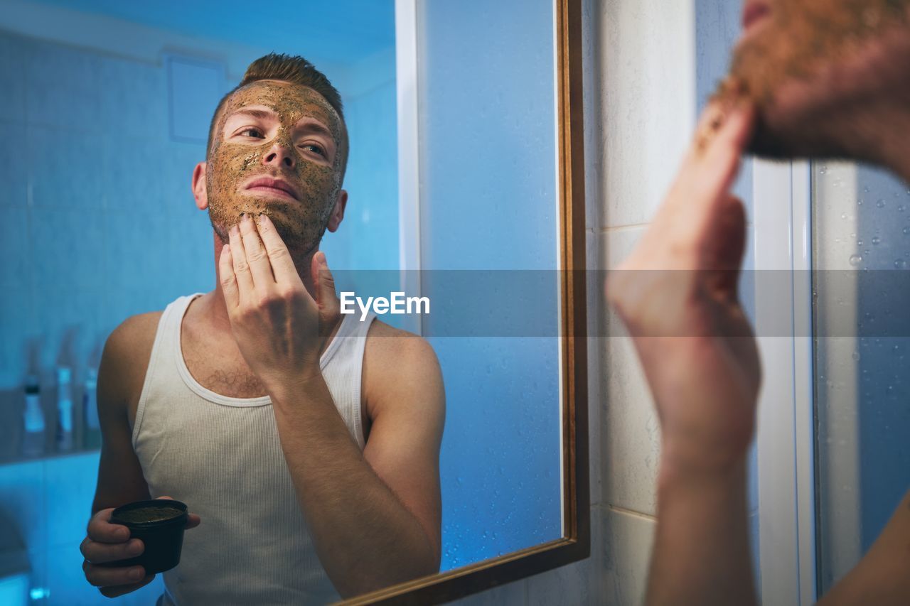 Man applying mask on face while looking in mirror at home