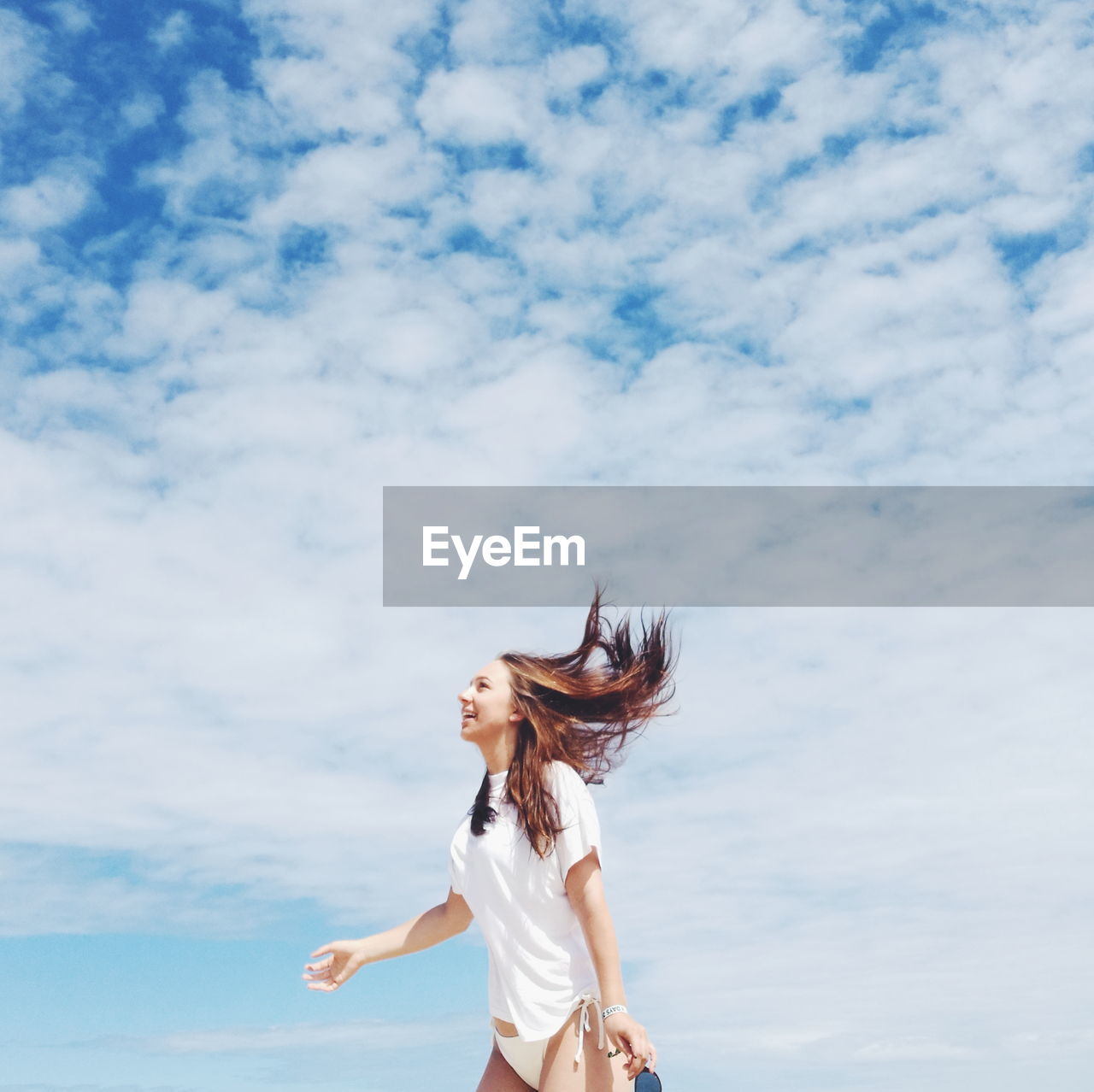 Smiling young woman standing against cloudy sky