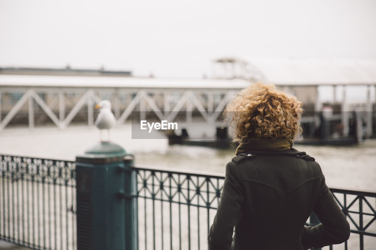 Rear view of woman with curly hair walking by railing against lake