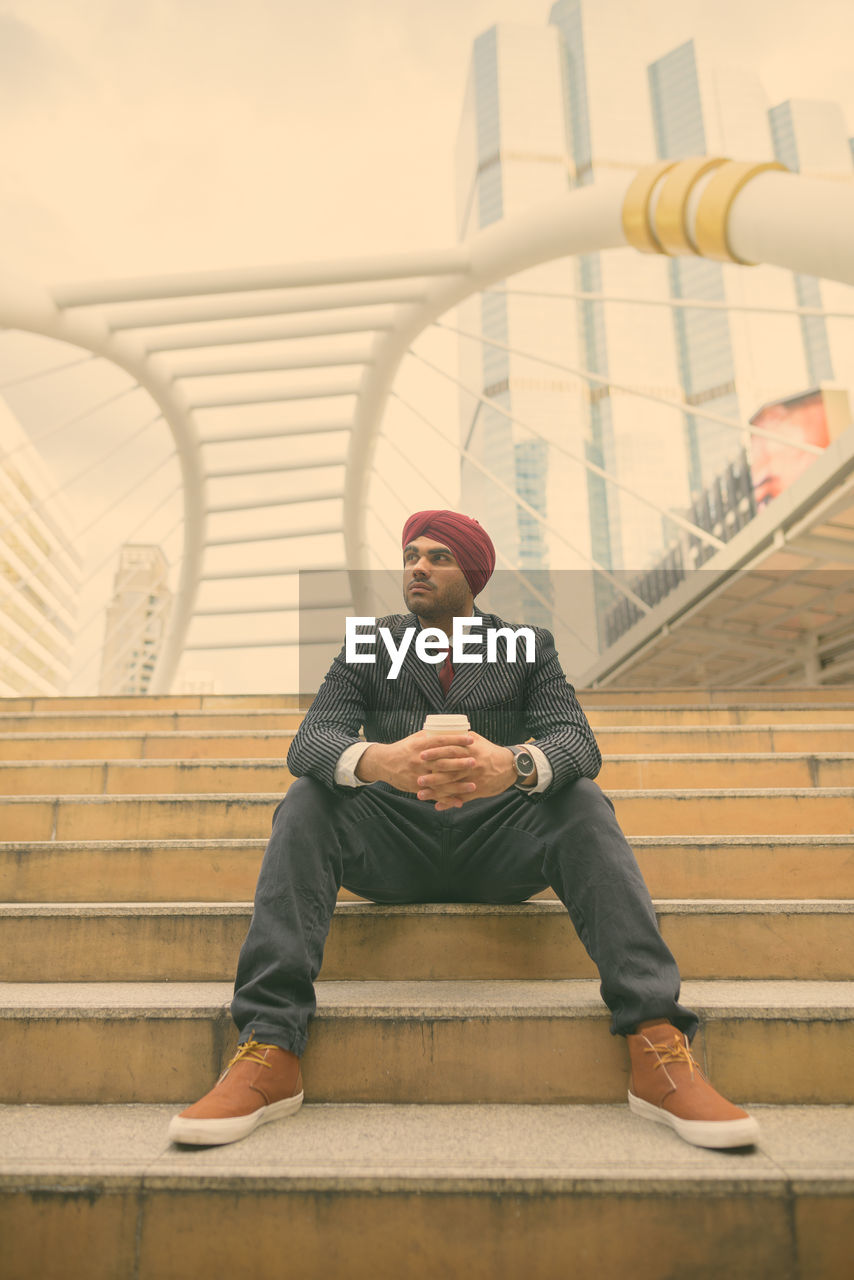 FULL LENGTH OF YOUNG MAN SITTING ON STAIRCASE