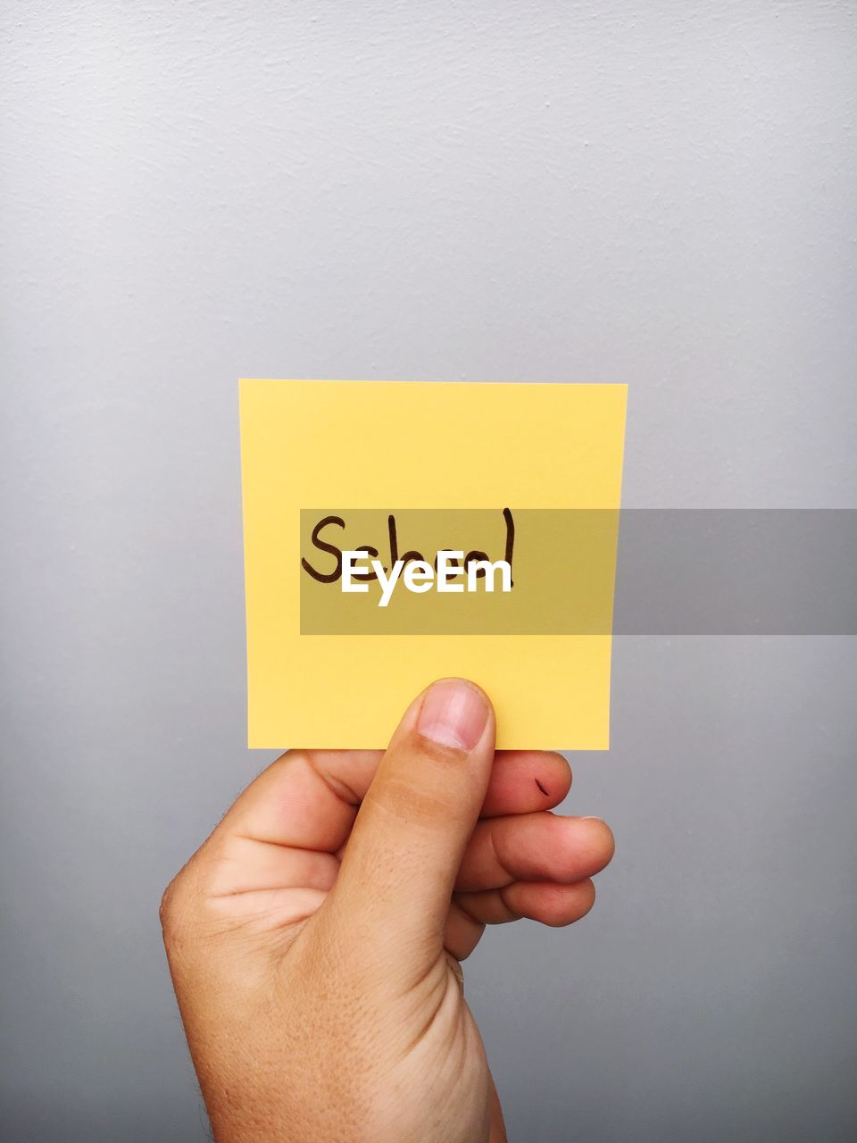 Cropped hand of person holding school text on adhesive note against gray background