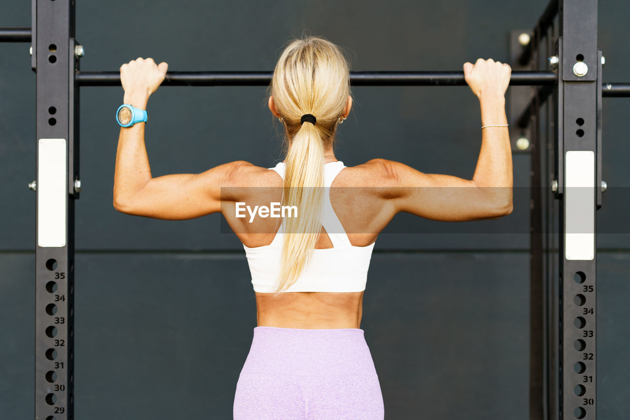 full length of young woman exercising with dumbbells at gym