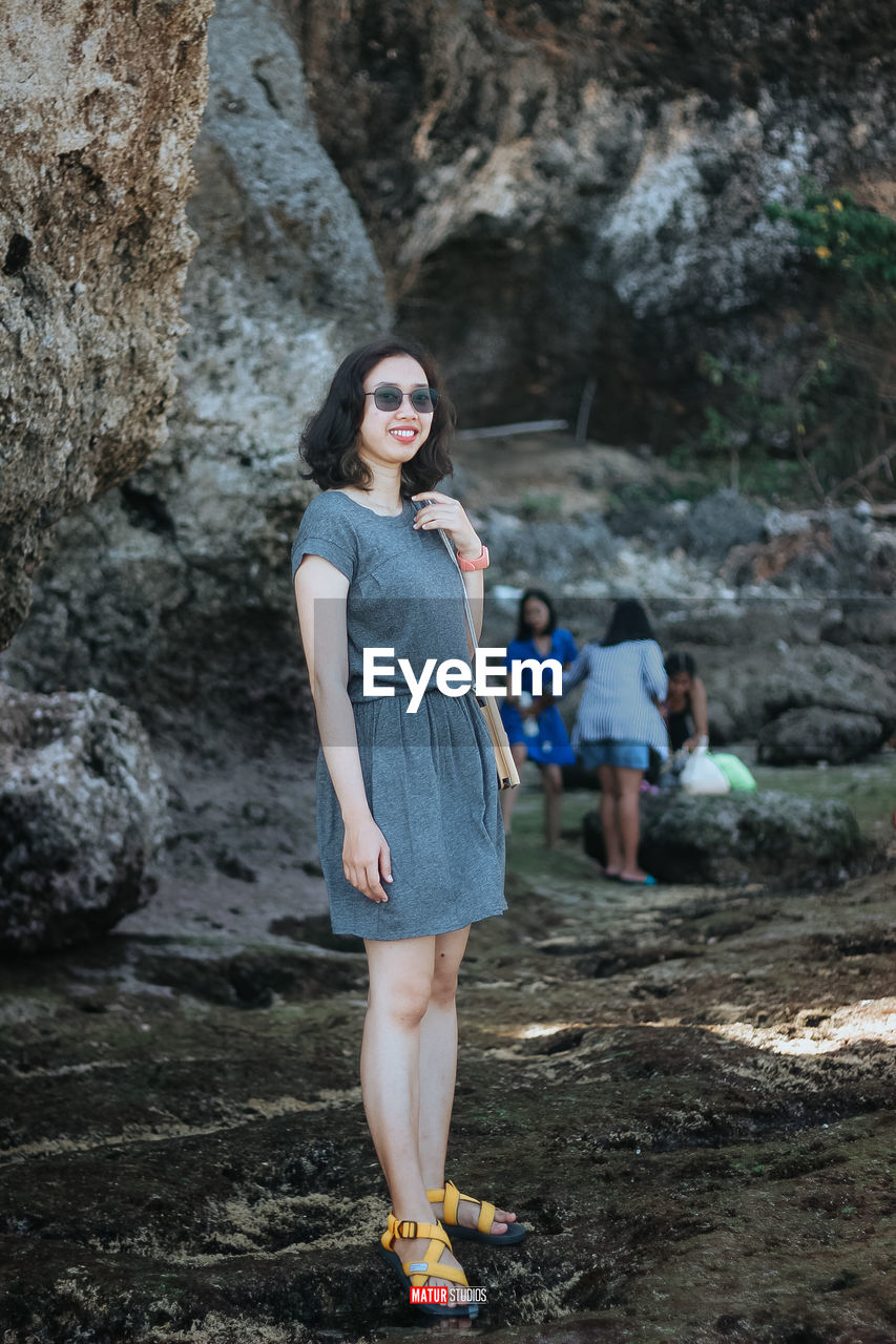 PORTRAIT OF YOUNG WOMAN STANDING ON ROCK