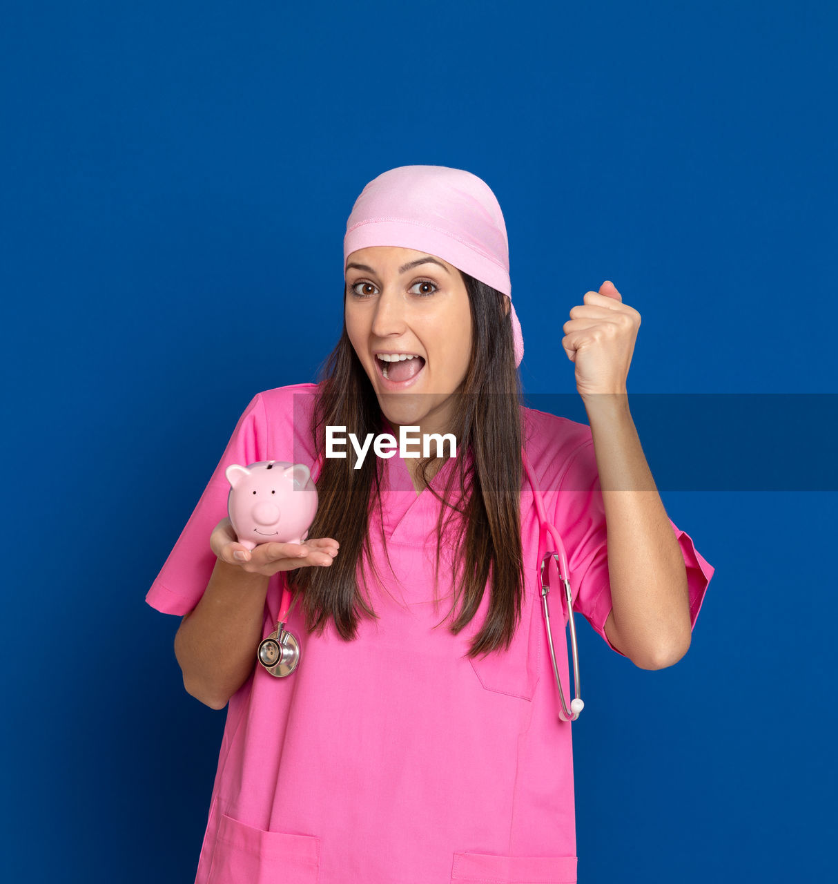 PORTRAIT OF SMILING YOUNG WOMAN STANDING AGAINST BLUE WALL