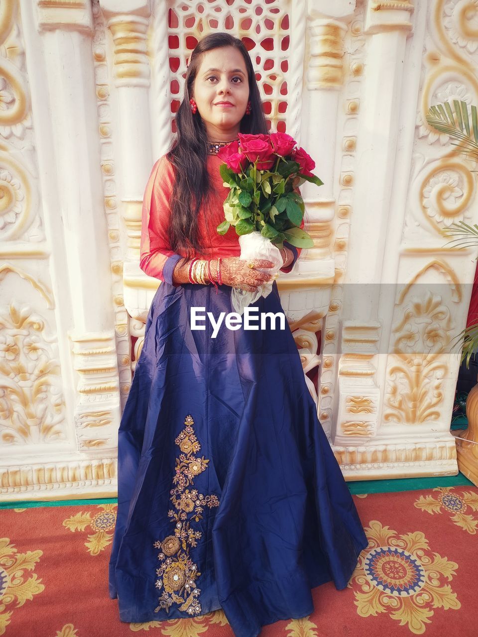 one person, bride, women, full length, clothing, adult, gown, dress, portrait, looking at camera, smiling, flower, indoors, wedding dress, formal wear, traditional clothing, young adult, elegance, standing, flowering plant, happiness, fashion, celebration, emotion, flower arrangement, plant, front view, event, female, bouquet, tradition, holding, quinceañera, brown hair, ornate, architecture, wedding, religion, lifestyles, flooring, pattern, sari, glamour, ceremony, life events, newlywed