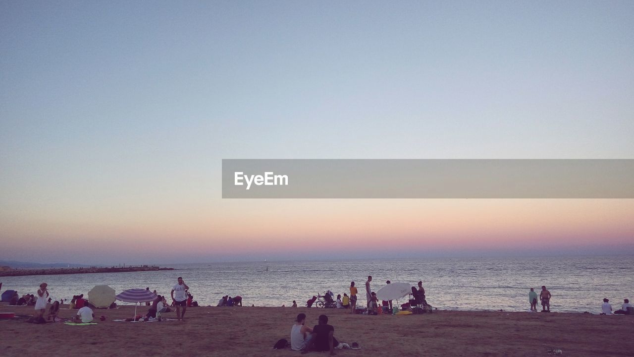 REAR VIEW OF PEOPLE ON BEACH AT SUNSET