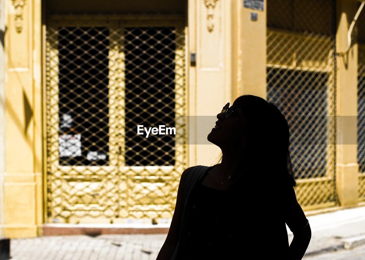 Silhouette of woman looking away while standing against building