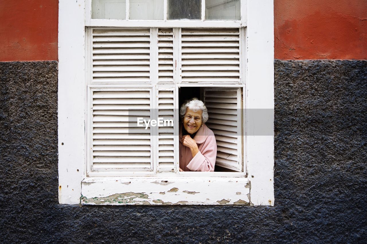 PORTRAIT OF HAPPY BOY AGAINST WINDOW OF HOUSE