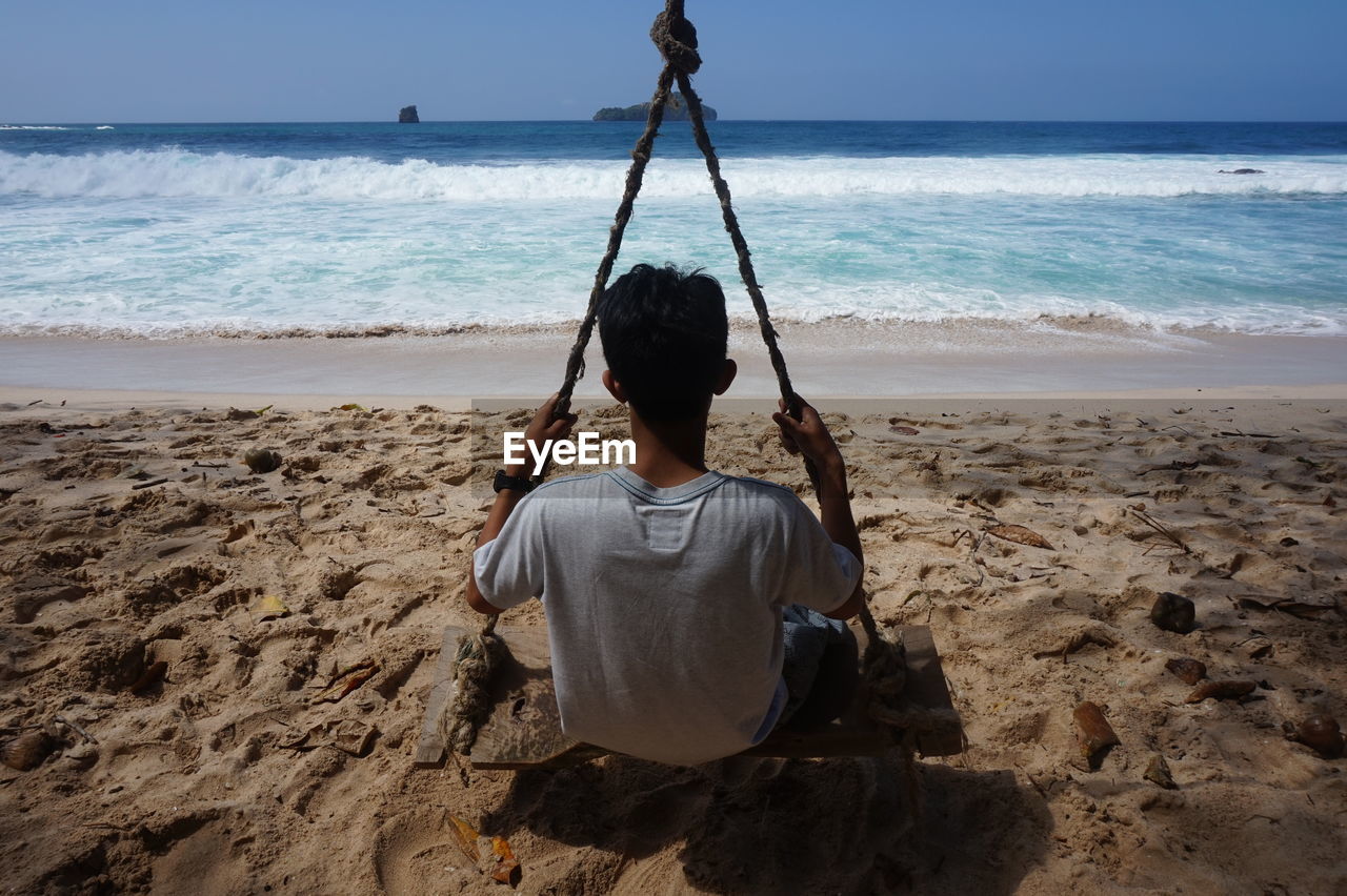 sea, land, beach, water, rear view, sand, sky, nature, shore, one person, ocean, horizon over water, horizon, coast, leisure activity, beauty in nature, scenics - nature, vacation, adult, lifestyles, body of water, holiday, motion, sitting, day, trip, men, wave, sunlight, outdoors, person, tranquility, relaxation, full length, women, clear sky, childhood, tranquil scene, casual clothing, sports, sunny