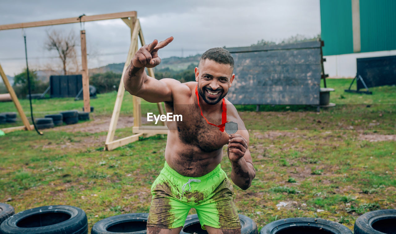 Portrait of shirtless man showing medal while exercising on land