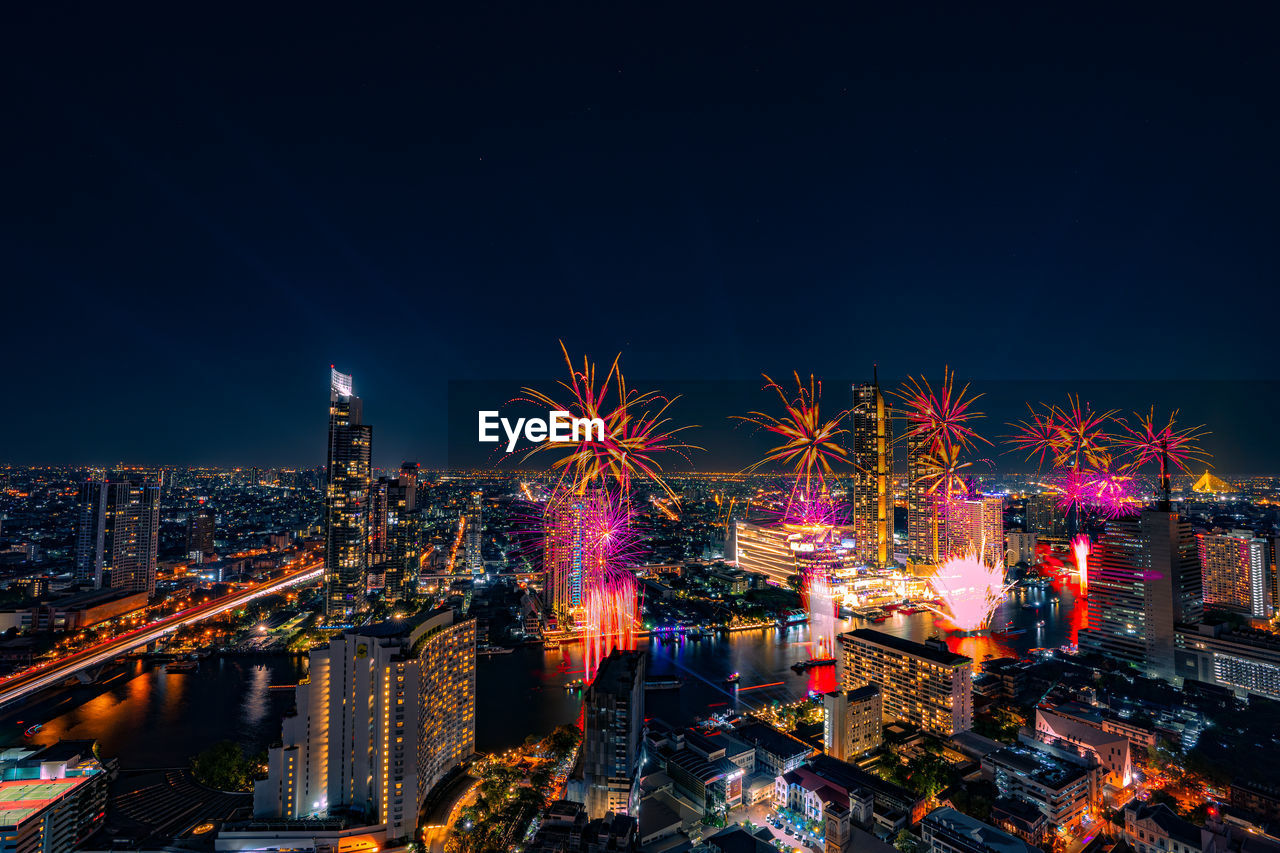 Firework display over city lit up at night. high angle view of illuminated buildings 