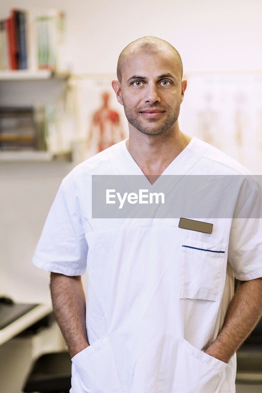Portrait of confident orthopedic surgeon standing with hands in pockets in clinic