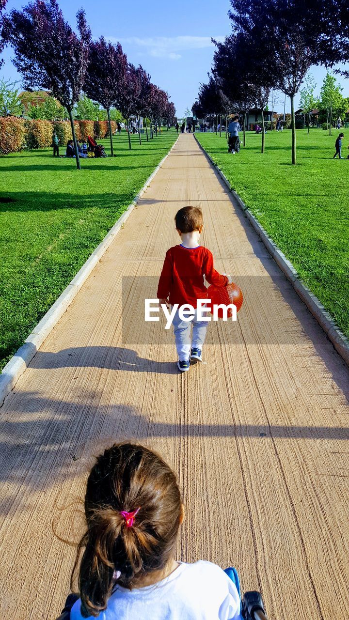 Siblings on footpath against trees in sunny day