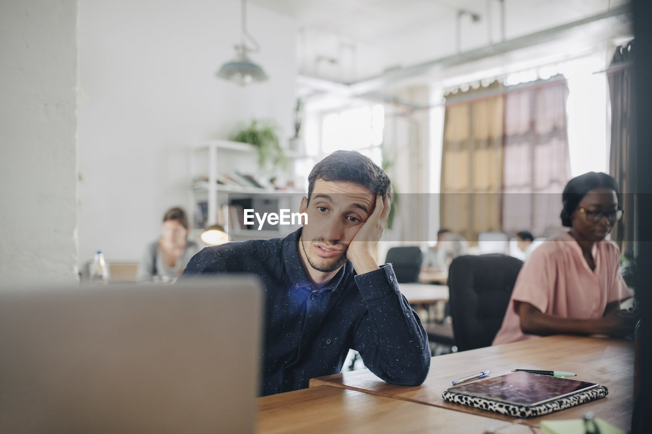 Tired businessman looking at laptop while sitting at desk in creative office