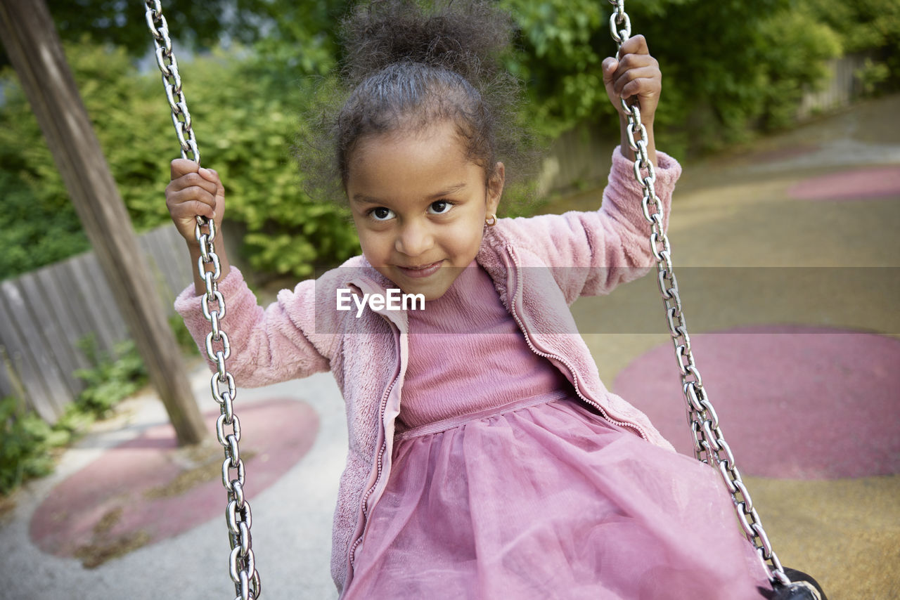 Happy girl having fun on swing in playground