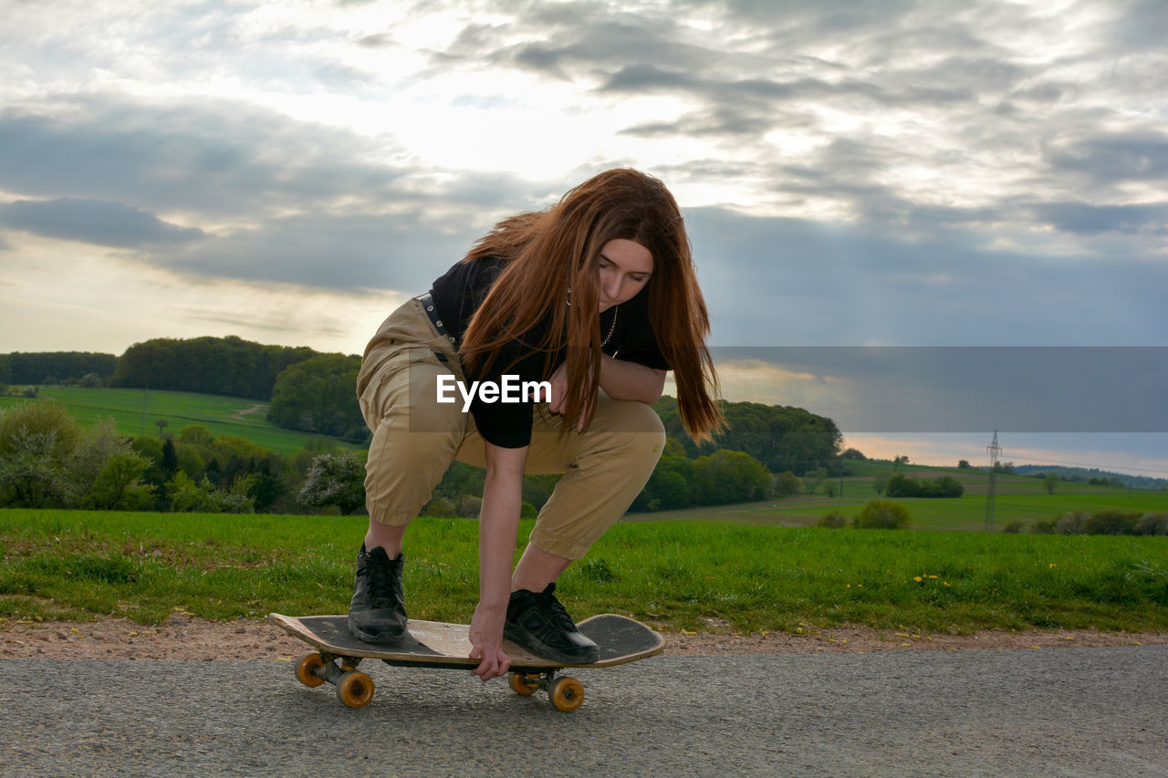 A young girl squats skateboarding on a road in green nature