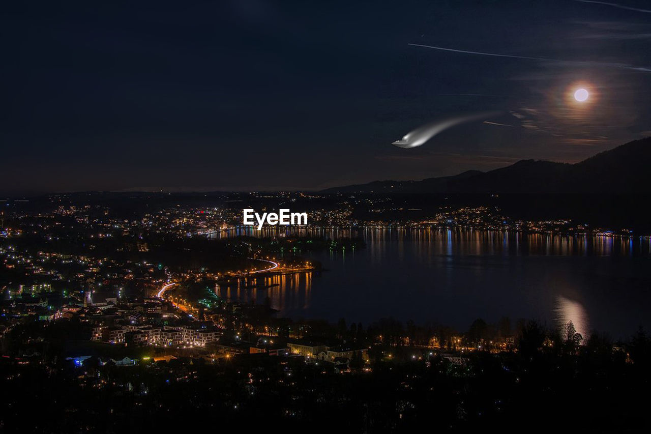 ILLUMINATED CITY BY SEA AGAINST SKY AT NIGHT