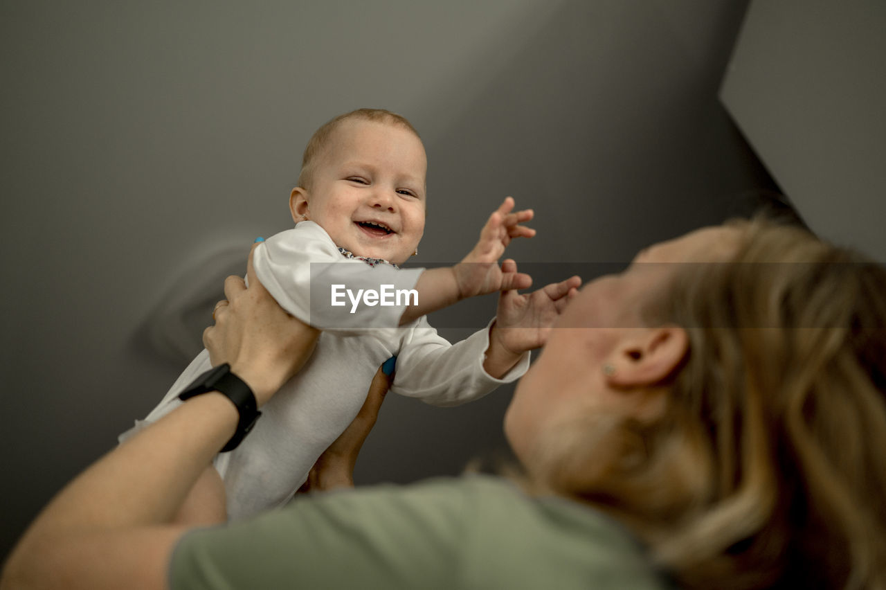 Mother lifting up happy baby girl at home