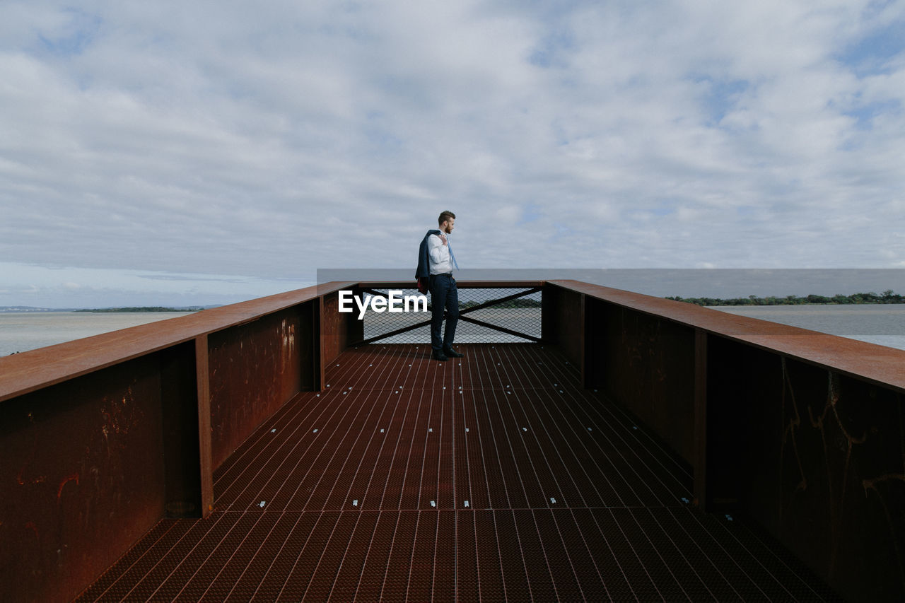 Man standing on bridge against sea