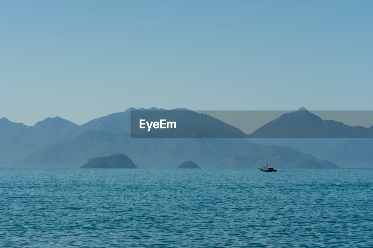 Scenic view of sea and mountains against clear sky