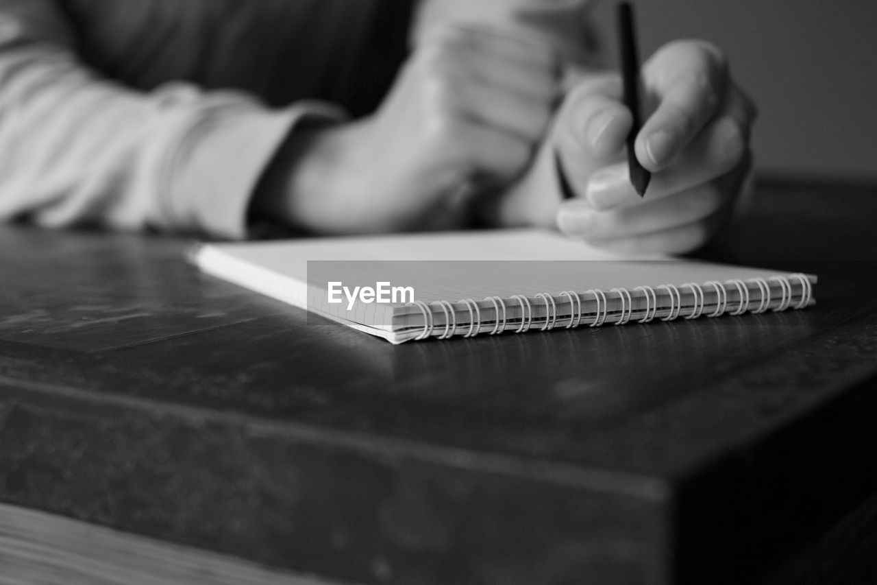 Midsection of person writing in book on table