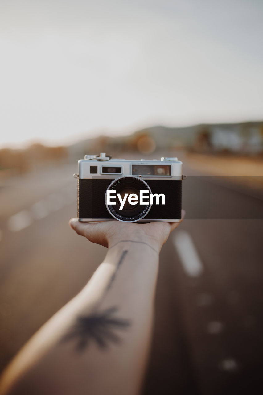 Crop hand of person with vintage camera on palm between asphalt route on blurred background