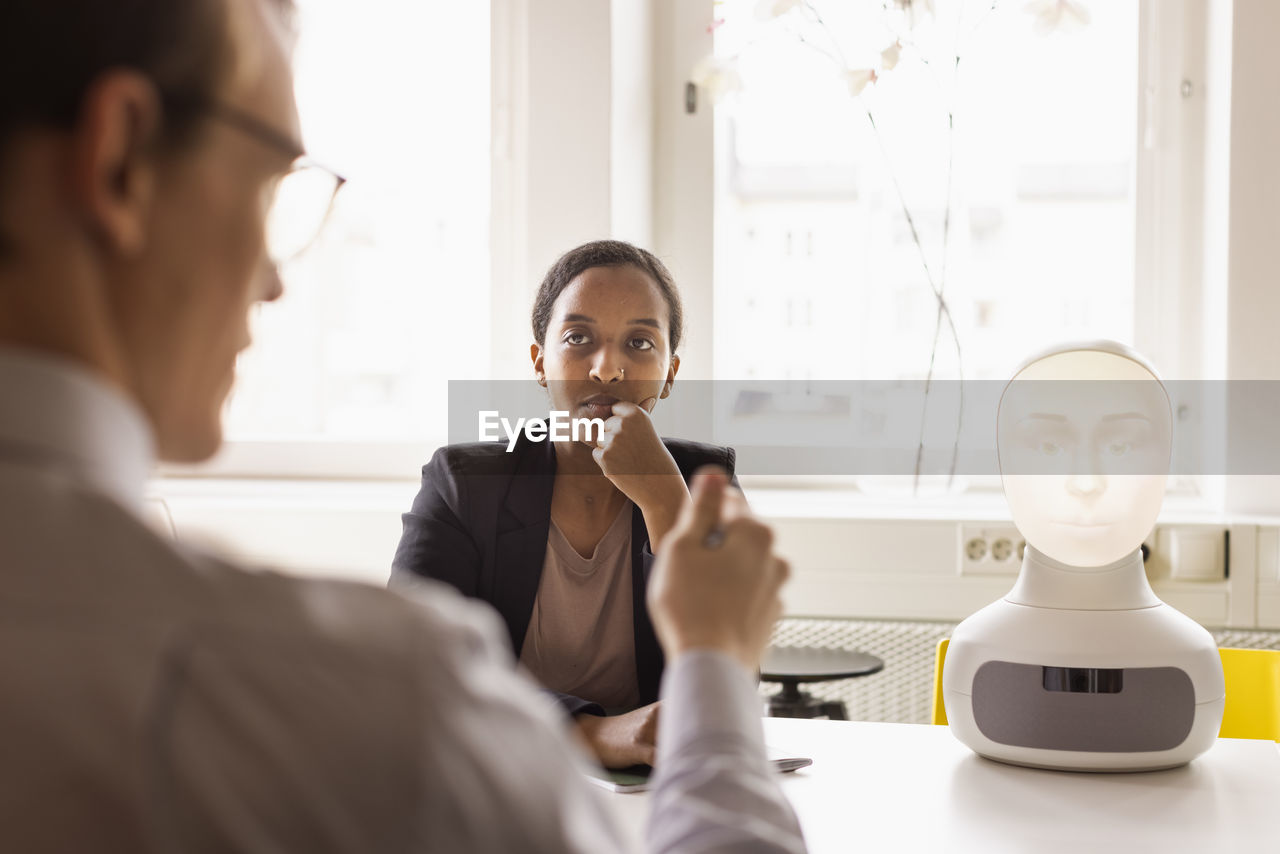 Business people discussing robot voice assistant during meeting