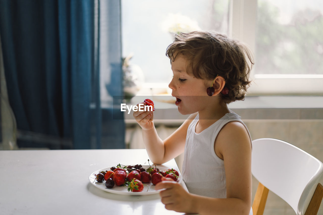 Cute beautiful little boy eating fresh cherry and strawberry.