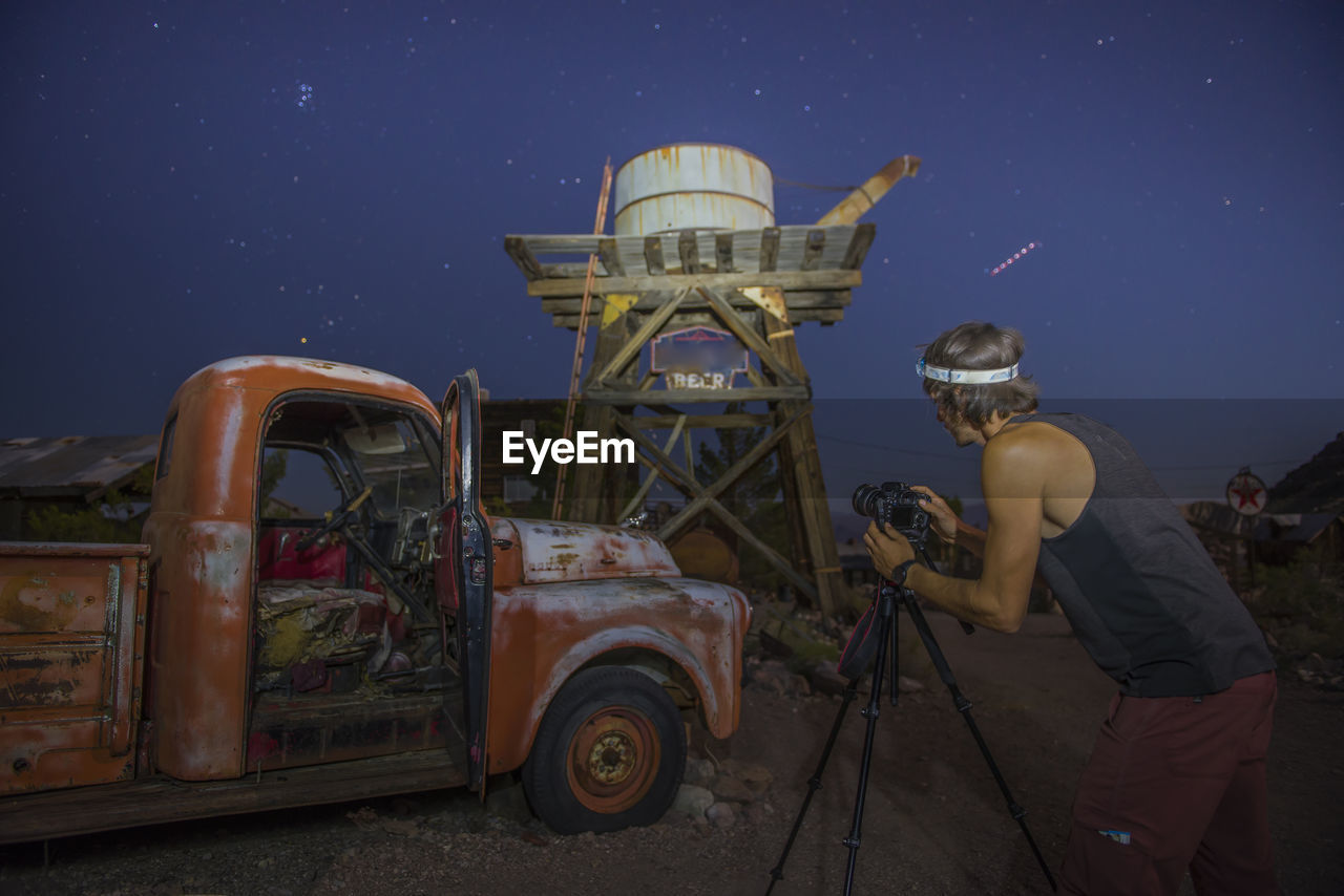 Young photographer capturing vintage car and water tank at night