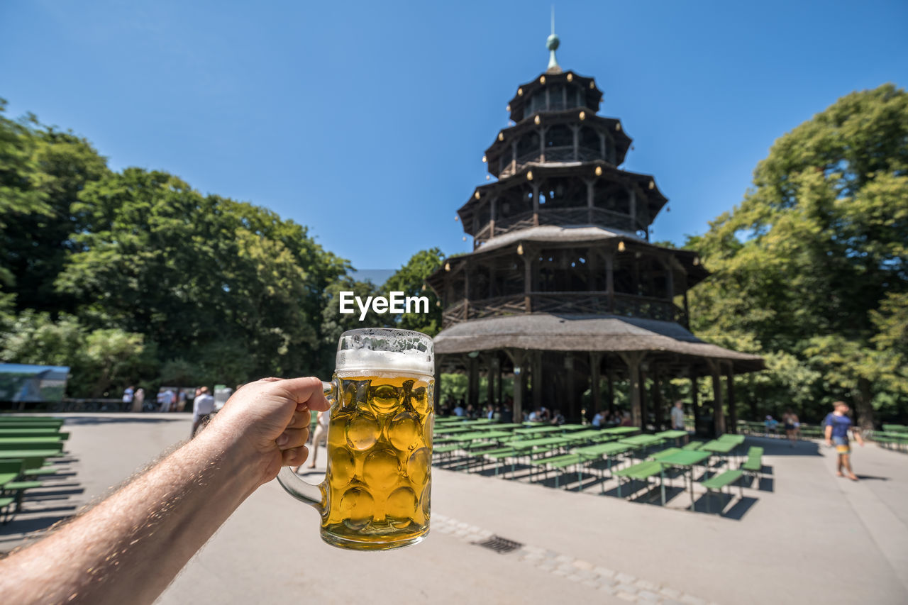 Cropped hand of man holding beer glass against clear sky