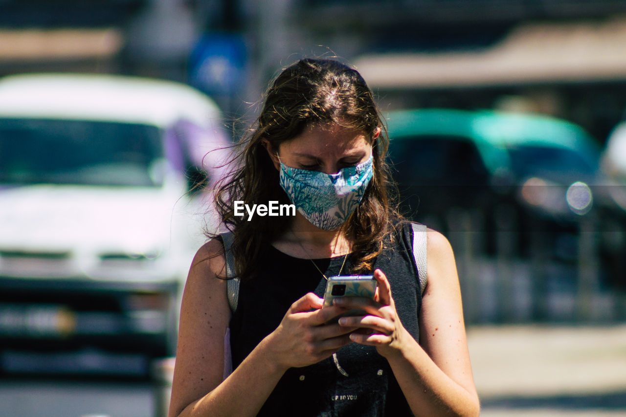 YOUNG WOMAN USING SMART PHONE WHILE PHOTOGRAPHING IN MOBILE