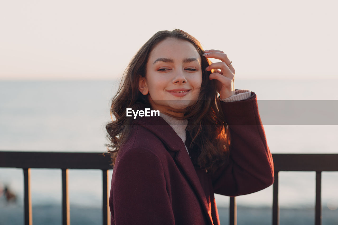 PORTRAIT OF SMILING WOMAN AGAINST SEA