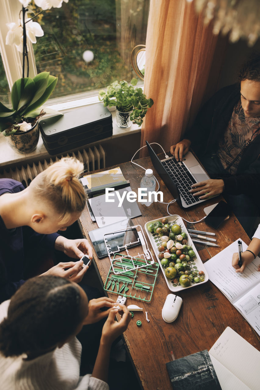 High angle view of friends working on project while teenager studying at table in house