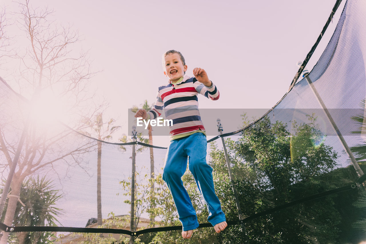 Low angle view of boy jumping on trampoline against trees