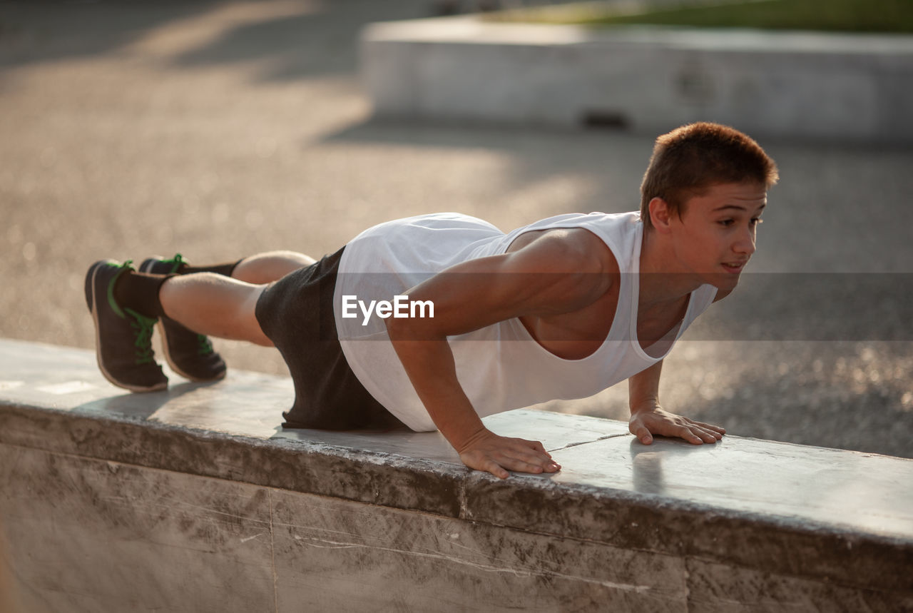 Side view of young man doing push-ups on retaining wall