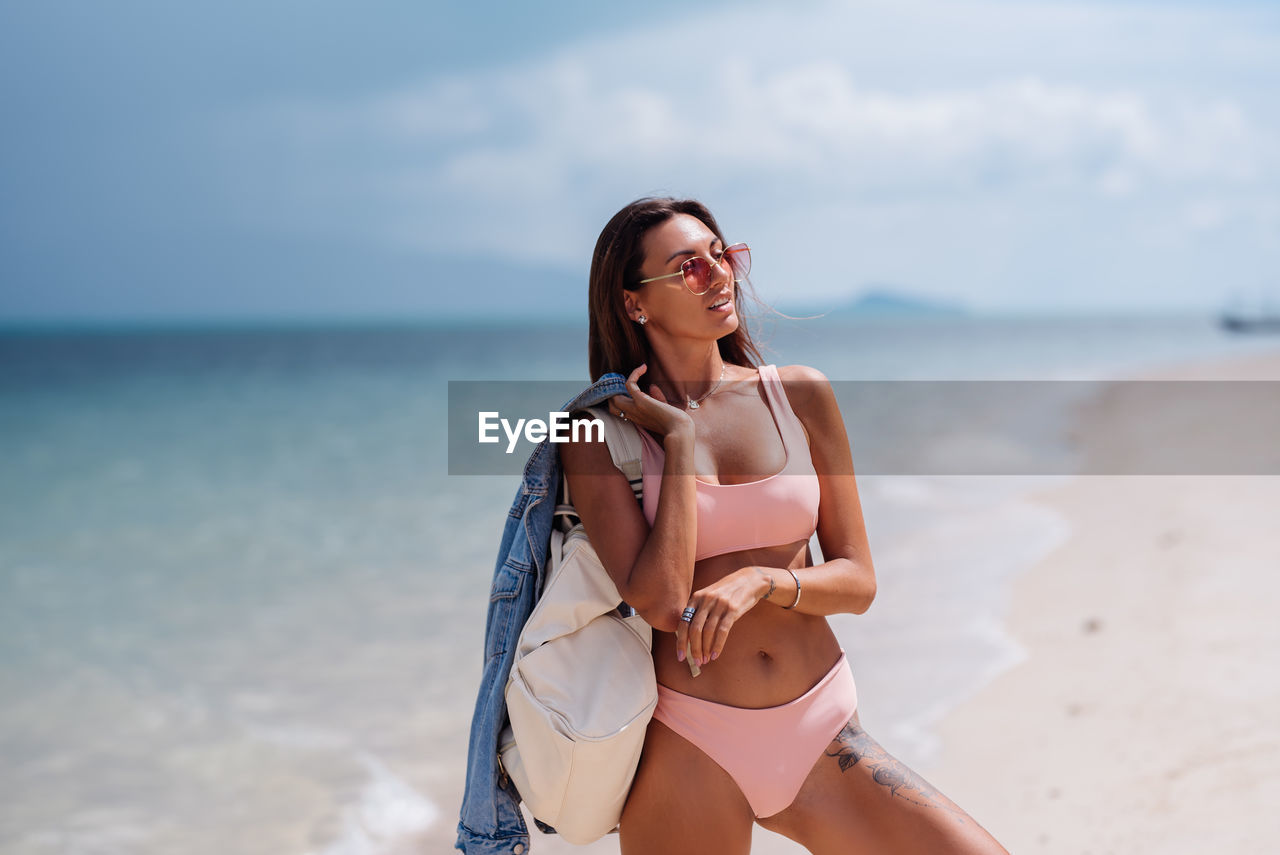 Young woman standing on beach against sky