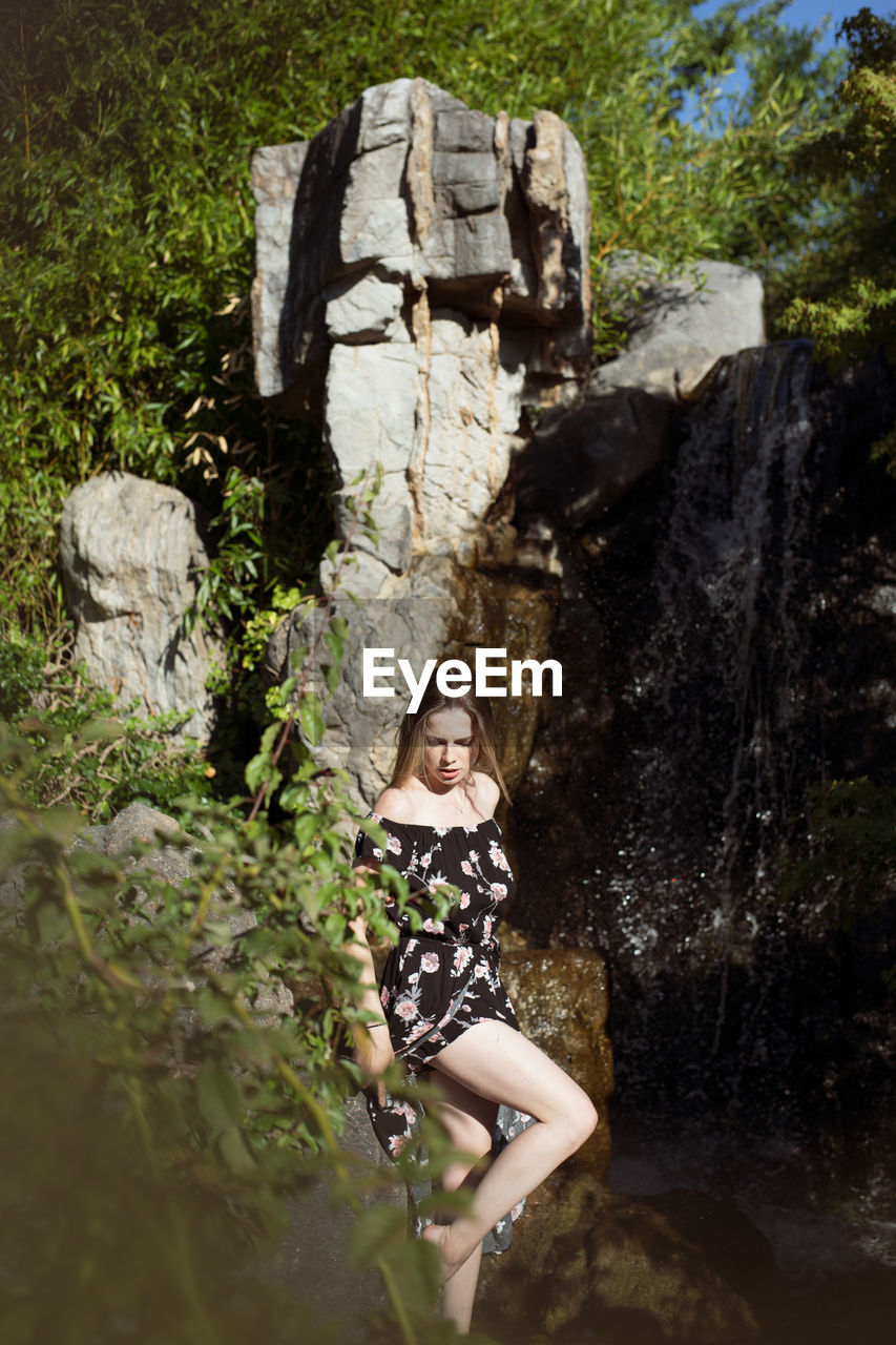 Portrait of young woman standing on rock by water