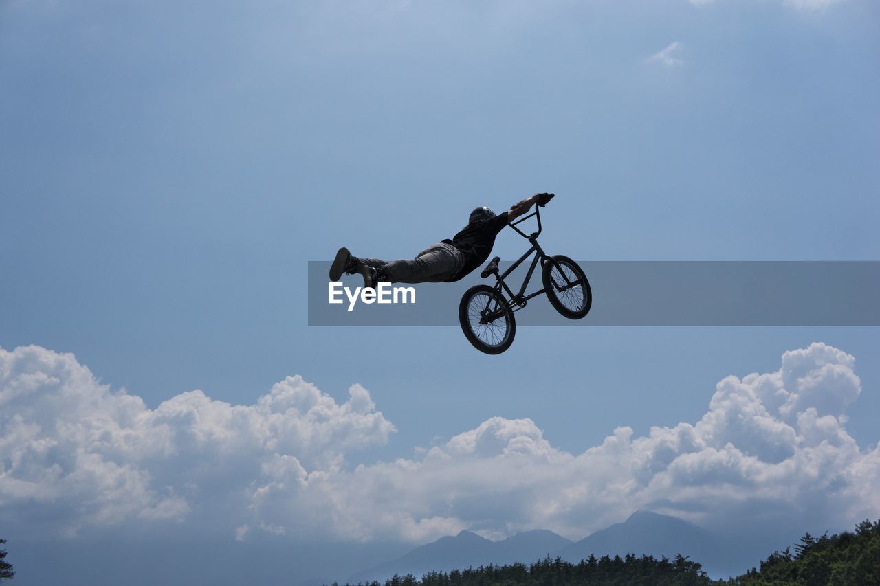 Low angle view of man with bicycle performing stunt against sky during sunny day
