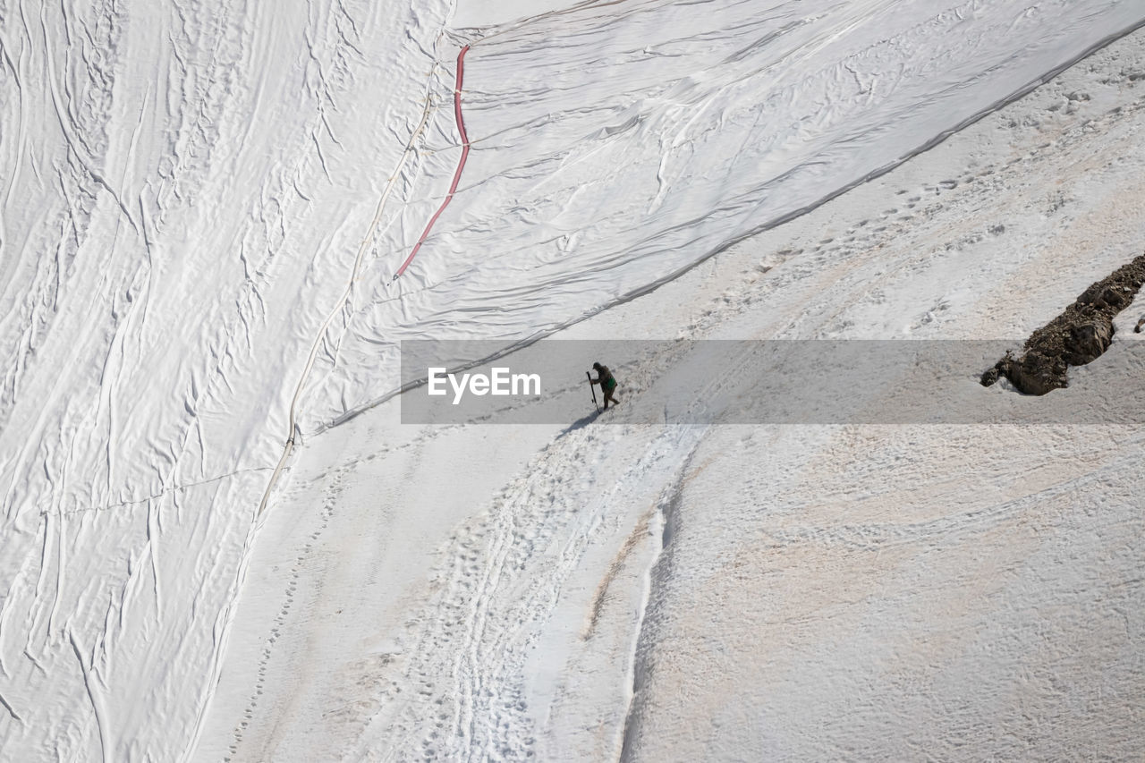 HIGH ANGLE VIEW OF PERSON SKIING ON SNOWCAPPED MOUNTAINS